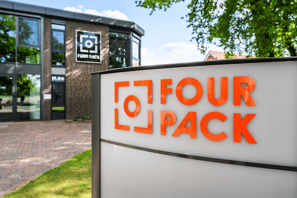 Firmenschild mit FOUR PACK Logo im Außenbereich vor Bäumen.