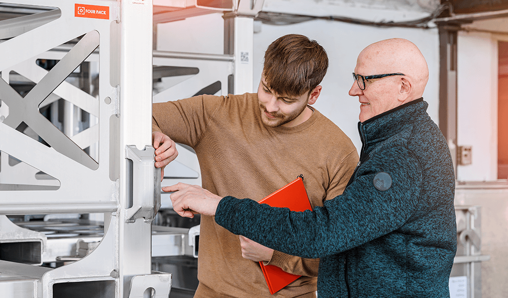 Zwei Mitarbeiter bei FOUR PACK besprechen Details an einer Transportlösung, einer hält einen roten Ordner.