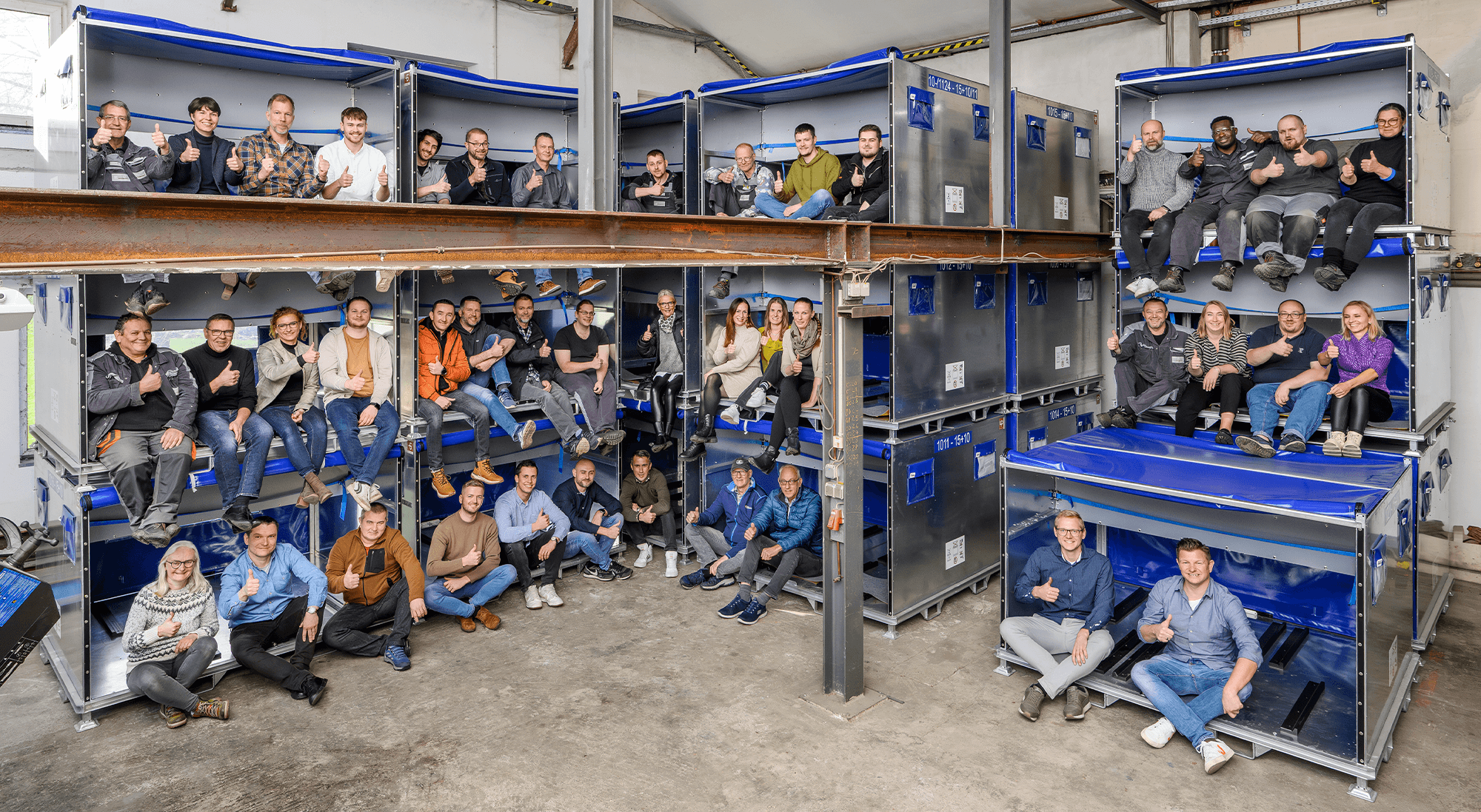 Gruppenfoto des FOUR PACK Teams, Mitarbeiter sitzen in mehreren gestapelten Containern.